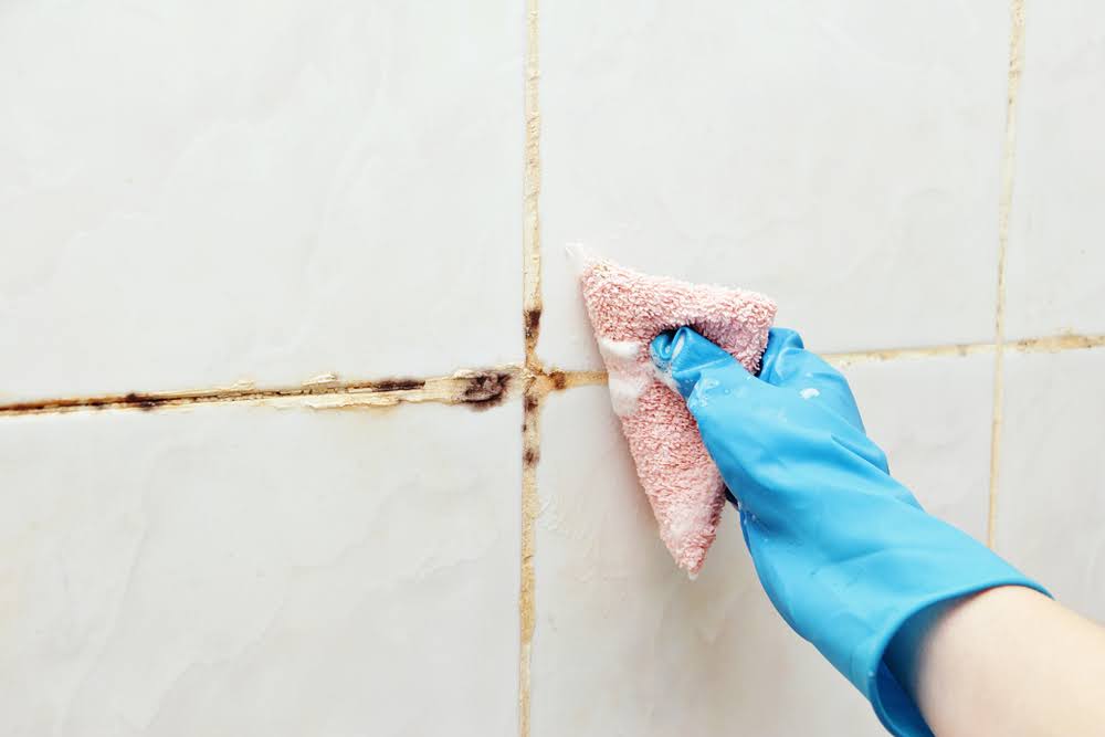 A person wearing cleaning gloves and removing mold from grout.